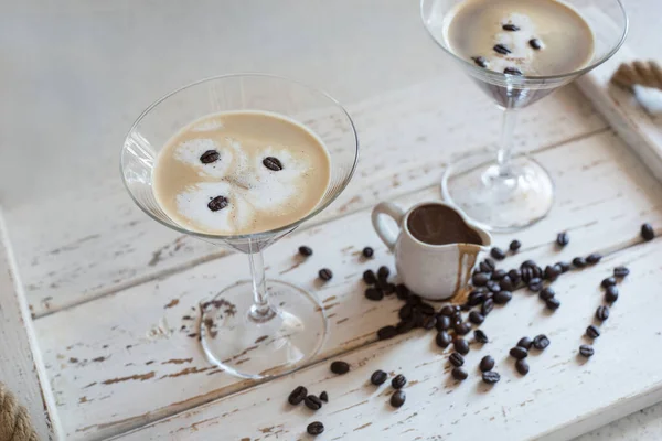 Espresso Martini cocktail in a martini glass decorated with coffee beans and a small jug with coffee liqueur in a bright interior