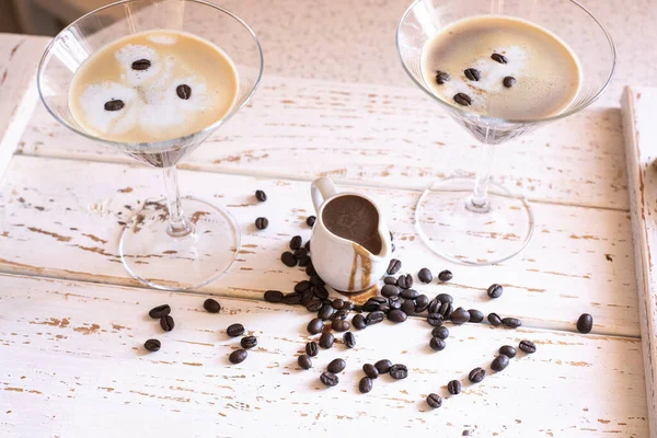 Espresso Martini cocktail in a martini glass decorated with coffee beans and a small jug with coffee liqueur in a bright interior
