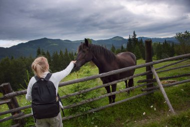 Bir kadın turist dağlarda at besliyor. Yeşil dağlar ve kozalaklı ormanlardan oluşan güzel bir dağ manzarası..