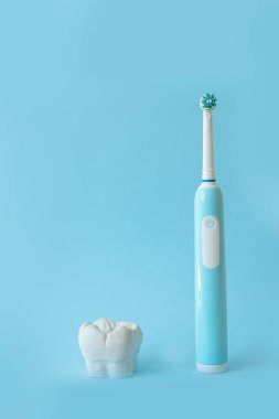 Mavi arka planda elektrikli diş fırçası ve diş modeli.