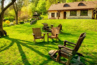 Baharda bir çiftlik evinin yanındaki eski ahşap sandalyeli yeşil çimenlikte rahat bir dinlenme yeri. Ukrayna