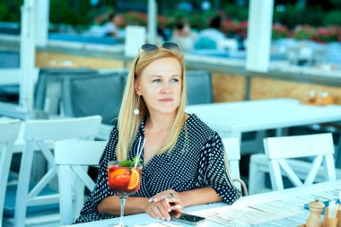 Düşünceli, sakin, sarışın bir kız caddedeki bir kafede sangria içiyor..