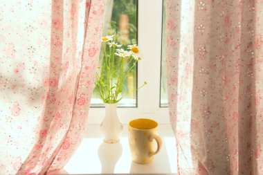 Sabah bir bardak su ve bir buket papatya. Küçük çiçekli perdelerin olduğu bir pencerede. Şirin Provence tarzı.