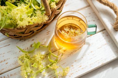 Şeffaf fincanda ıhlamur çayı ve ıhlamur çiçekleri var..