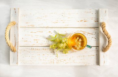  Hafif bir arka planda beyaz bir ahşap tepside ıhlamur çayı ve ıhlamur çiçeği. Düz üst görünüm.