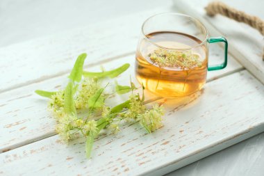 Şeffaf fincanda ıhlamur çayı ve ıhlamur çiçekleri var..