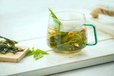  Isırgan kökleri ve açık arkaplanda yaprakları olan cam bardak.