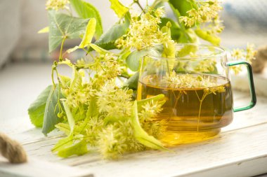 Şeffaf fincanda ıhlamur çayı ve ıhlamur çiçekleri var..