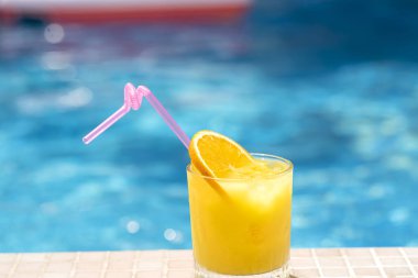 Bir bardak portakallı limonata ve arka planda mavi havuz suyu olan buz.