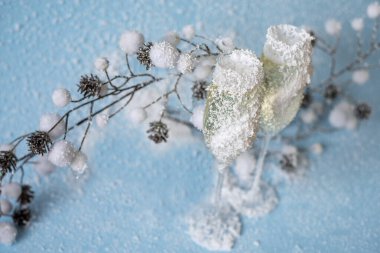 Açık mavi arka planda beyaz yapay karda iki bardak şampanya. Yeni yıl arkaplanı.