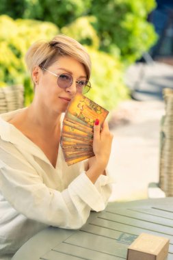 A woman sits at a table with tarot cards in her hands and smiles. astrologer, tarot reader. clipart