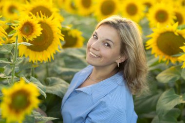 Güneş batarken sarı ayçiçeği tarlasında gülümseyen mutlu kadın. Gerçekten basit bir kadın. Model değil, rötuş yapmadan.