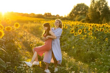 Anne ve kızı gün batımında güneş batımında bir kır yolunda ayçiçeği tarlasında oynaşıyorlar. Gerçek hayat.