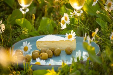 Papatya otlağında bir tabak peynir, zeytin ve şampanya. ruh hali yaz ve doğa.