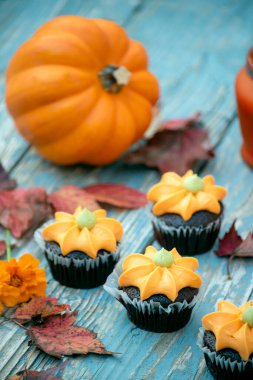 Balkabağı kremalı kekler, mavi ahşap arka planda mum ve renkli sonbahar yaprakları. Sonbahar bayramı Cadılar Bayramı ve Şükran Günü.