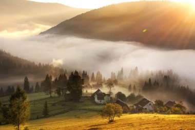 Dağlarda muhteşem bir gün doğumu. Dağın arkasından gelen güneş ışınları vadideki küçük evleri aydınlatıyor ve yoğun sis..