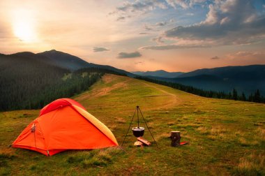 Orange tent on a meadow in the mountains at sunset. Cooking tent with a cauldron. clipart