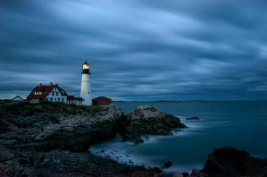 Okyanus kıyısındaki bir deniz fenerinin karanlık dramatik fotoğrafı. Gece fotoğrafı. Dramatik gökyüzü. Bulutların akışını ve donmuş suyun hareketini gösteren uzun bir pozlama. Portland Baş Işığı