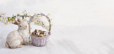 Küçük bir sepetin içinde yumurtalar, tavşan heykelciği ve arka planda çiçek açan kiraz dalı. Pankart. Boş yer. bahar Paskalya arkaplanı.