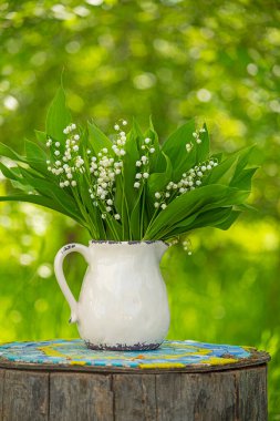 Bahar çiçekleri, yeşil bir bahçede seramik bir sürahi içinde vadideki zambaklar..