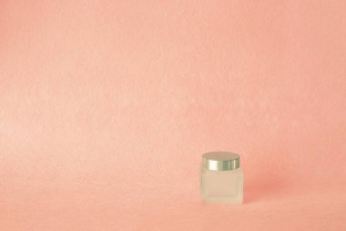 Pembe arka planda cam bir krema kavanozu. Yüz ve vücut bakımı konsepti. Model modeli. Boşluğu kopyala, 
