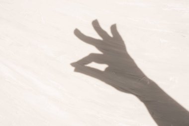 Açık dokulu bir yüzeye iki parmağıyla yapışan bir elin gölgesi. Zarafet, dans. Boşluğu kopyala 