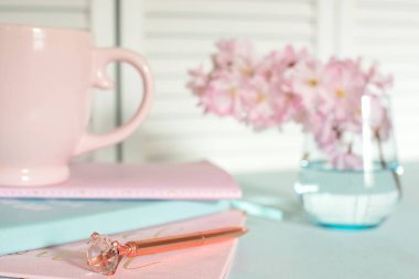 defterler, fincan, günlük, pastel mavi bir masaya yerleştirilmiş pembe sakura çiçekleri. Sahne sakin, stil ve yaratıcılık dolu, iş ve yaratıcılık için ideal..