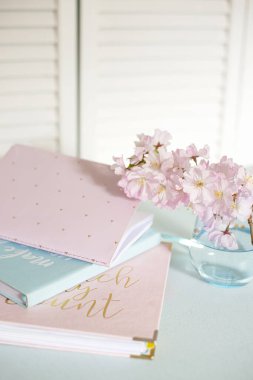 Not defterleri, günlük, pastel mavi bir masaya yerleştirilmiş pembe sakura çiçekleri. Sahne sakin, stil ve yaratıcılık dolu, iş ve yaratıcılık için ideal. Üst Manzara. Boşluğu kopyala 