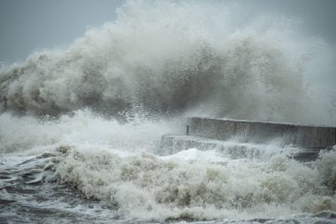 Fırtına sırasında büyük dalgalar beton iskele denizine çarpıyor. Bulutlu dramatik hava, sıçramalar, gri hava, doğanın gücü..