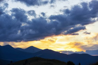 Dağ tepelerinin siluetleri dramatik günbatımı gökyüzüne karşı.