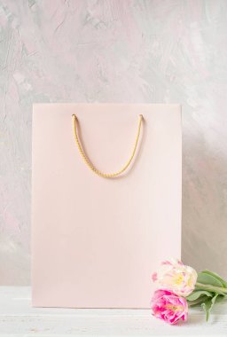 Pembe bir kese kağıdı ve lale çiçekleri açık gri-pembe arka planda macun desenli. Modelleme. Boş alan