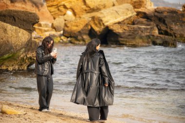 Sıcak bir aile anı anne ve kız şık deri ceketler içinde sahilde yürüyüş yapıyorlar. Beachamong 'da yürürken ve resim çekerken resimli kayalar, özgürlüğü, uyumu ve 