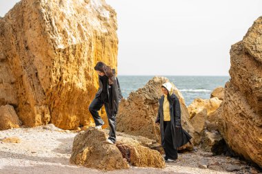  Aynı tarz siyah deri ceketleri giyen bir anne ve kız aktif olarak deniz kıyısındaki kayaların arasında yürüyorlar..