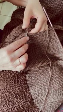 Kadın elinin iplikten örgü ördüğü kahverengi bir kazak. Detaylı yavaş el işi, yaratıcı el yapımı süreç, rahat ve sıcak işçilik.