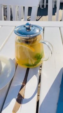 Şeffaf çaydanlık, portakal ve naneli çay, yakınlarda dizüstü bilgisayar, beyaz ahşap masa üzerinde yumuşak, yumuşak, yumuşak güneş ışığı...