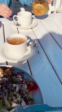 Bir kadının eli şeffaf bir çaydanlıktan şeffaf ahşap bir masada bir fincana portakallı ve nane şekerli aromatik çay döker. Yumuşak güneş ışığı rahat ve huzurlu bir ortam yaratır..