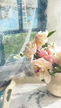 Pencerenin yanındaki eski bir köy verandasında vazonun içindeki pastel renkli şakayıklardan oluşan bir buket. Bir barış atmosferi ve kırsal yaşamın ahengi