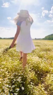 Açık renk kısa elbiseli, elinde papatya buketi ve hasır şapkalı bir kız uzaktaki bir tarlaya atlayıp papatyalarla çiçek açıyor..