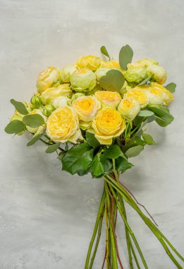  Bir buket soluk sarı şakayık tarzı gül, gri bir duvara karşı macun rengi ve mermer bir efektle. Düğünler, doğum günleri ya da özel günler için zarif bir çiçek hediyesi. 