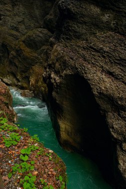  Almanya, Bavyera 'daki Partnachklamm Boğazı' nın gizemli fotoğrafı, zümrüt yeşili su, yosun kaplı uçurumlar, ve atmosferik, dramatik doğal manzara.