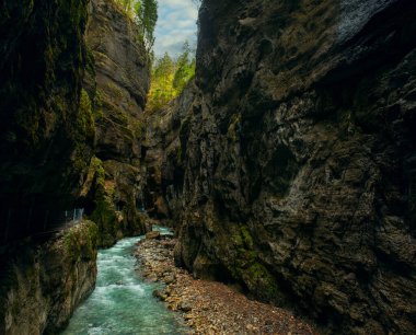 Almanya, Bavyera 'daki Partnachklamm Gorge' un gizemli fotoğrafı, zümrüt yeşili su, yosun kaplı uçurumlar, ve atmosferik, dramatik doğal manzara. dikey Panorama