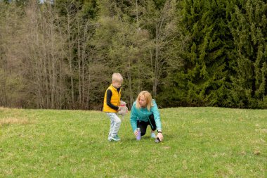 Genç bir büyükanne ve torunu yeşil bir dağ çayırında bitkileri keşfedip gözlemliyor. Aile bağlantısı, doğa eğitimi ve huzurlu bir kırsal an..