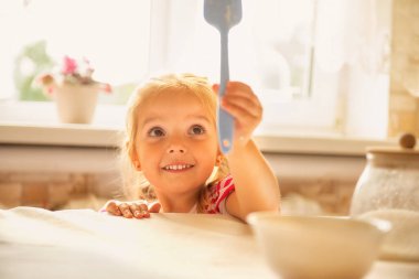 Sevimli küçük kız mutfakta yardım ediyor, ailesiyle yemek pişirirken gülümsüyor. Mutlu çocukluk kavramı, aile gelenekleri, birlikte yemek pişirme ve ev hayatı. Ebeveynlik, yemek hazırlama, eğitim ve neşeli çocukluk temaları için mükemmel bir imaj.