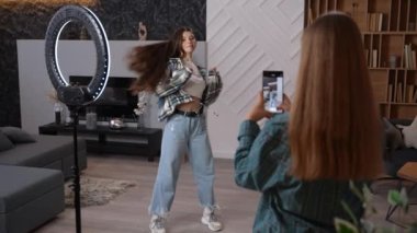 Genç ve çekici bir kadın, evinde ya da stüdyoda cep telefonuyla hip hop dansı yapan arkadaşını vuruyor. Sosyal medya için içerik oluşturan mutlu arkadaşlar. 4K yüksek kaliteli görüntü