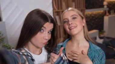 Güzel genç kadınlar cep telefonu kamerasıyla selfie çekiyor. Arkadaşlar mutlu bir şekilde gülümsüyor, evde kameraya poz veriyorlar. Sosyal medya için içerik oluşturan güzel kızlar. Yüksek kaliteli görüntüler