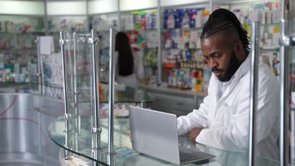 这个4K高质量的库存视频展示了在药店缓慢工作的深色皮肤中年男性药剂师在笔记本电脑上的工作 重点是医疗和医药 — 图库视频影像