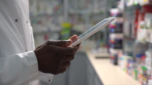 アフリカ系アメリカ人の男性薬剤師の手の4K映像を専門的に撮影し デジタルタブレットPcを使って医薬品パッケージを監査することで ドラッグストアスタッフの重要な仕事を探る — ストック動画