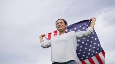 Amerikan bayrağını havada tutan neşeli melez kadın Bağımsızlık Günü 'nü çeşitli bir toplumda gurur ve mutlulukla kutluyor. 4k 