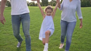Parkta mutlu bir çok ırklı aile bağı, yazın el ele tutuşmak, sallanmak, sevgi göstermek, ebeveynlik, birliktelik. 4k 