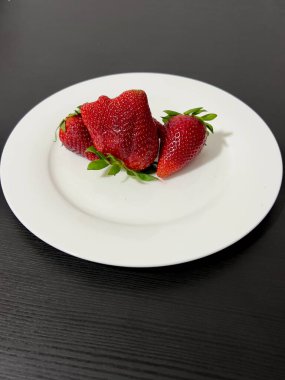 Siyah bir masada duran büyük çilekler..